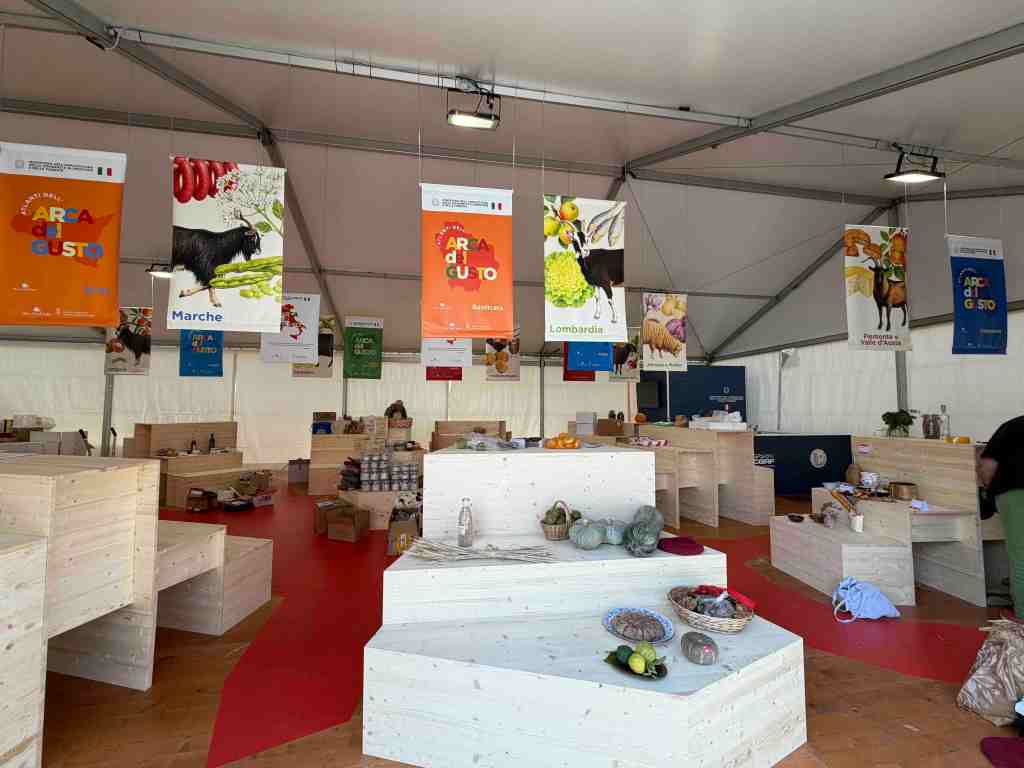 Interno di un mercato con stand in legno, decorato con banner delle regioni italiane e vari prodotti alimentari in esposizione.