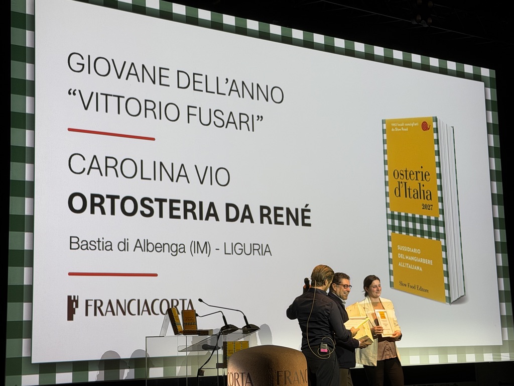Premiazione del Giovane dell'Anno "Vittorio Fusari" a Carolina Vio, rappresentante dell'Ortosteria da René di Bastia di Albenga, Liguria. In sottofondo, una presentazione del libro 'Osterie d'Italia 2027'.