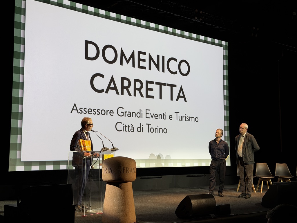 Un evento pubblico con Domenico Carretta, Assessore Grandi Eventi e Turismo della Città di Torino, sul palco con due persone presenti.