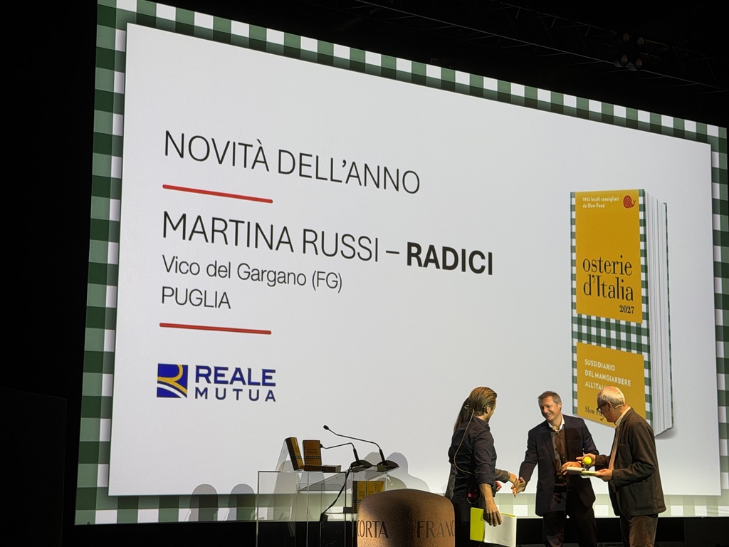 Presentazione del premio per la novità dell'anno a Martina Russi per 'Radici', accompagnata da un'immagine del libro 'osterie d'Italia 2027'.